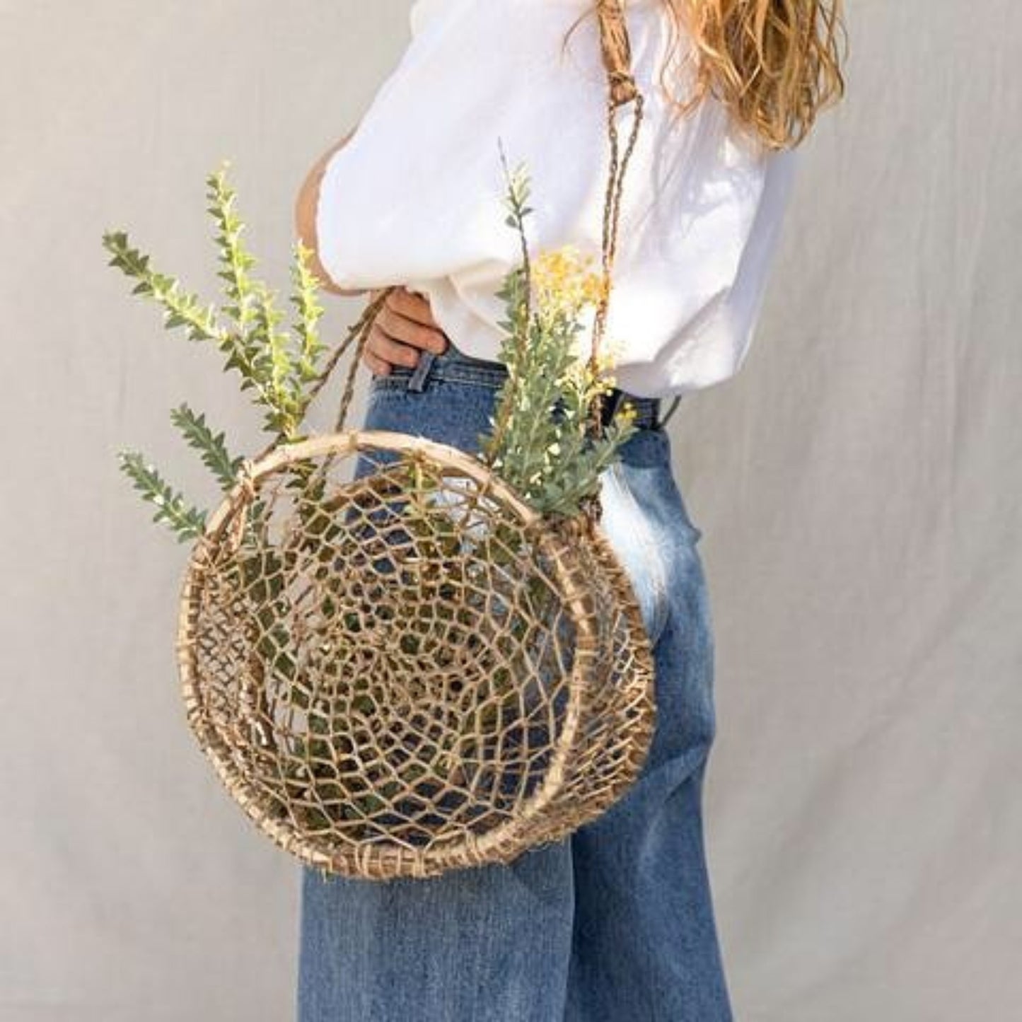 Handwoven circular jonote fiber basket bag worn over the shoulder with natural greenery