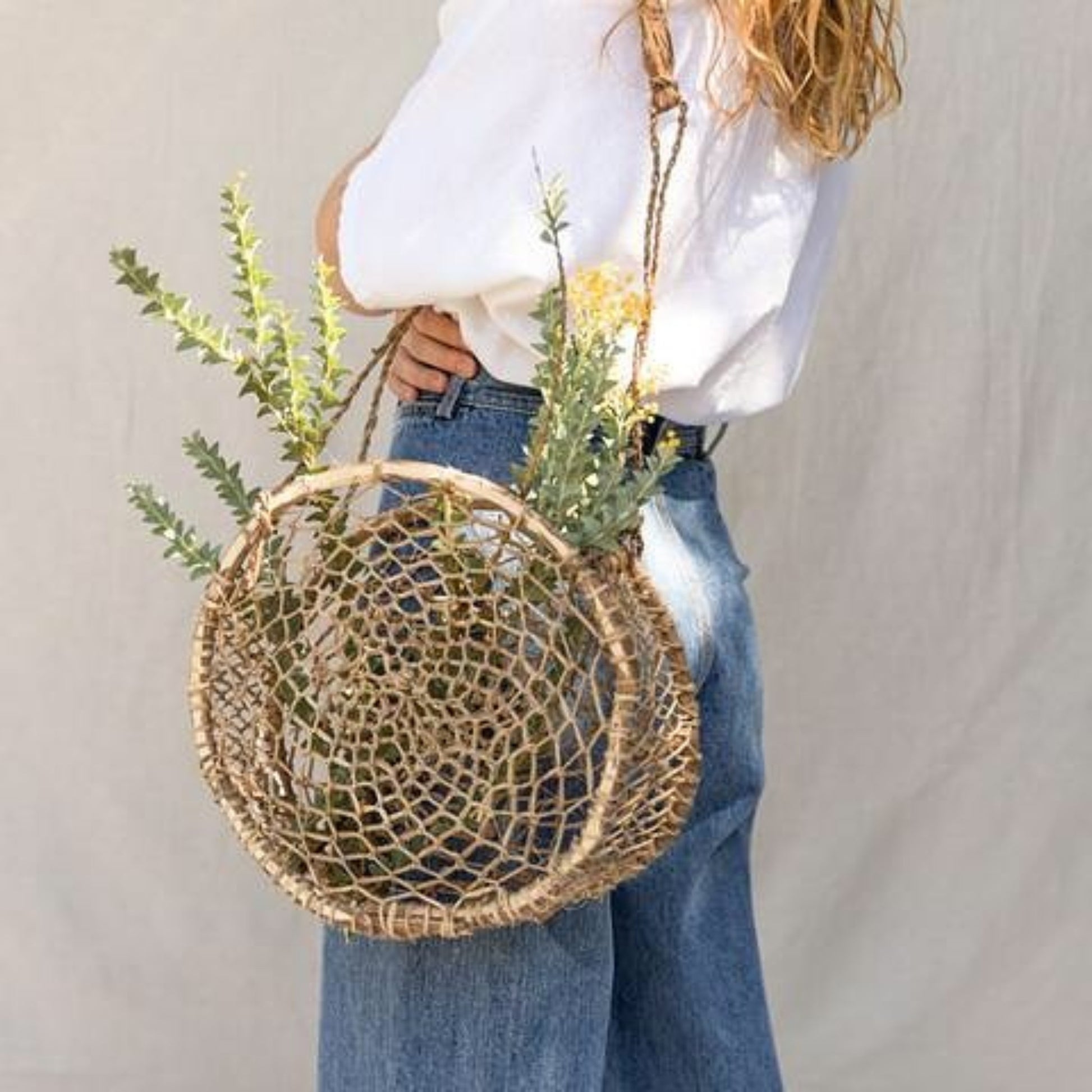 Handwoven circular jonote fiber basket bag worn over the shoulder with natural greenery