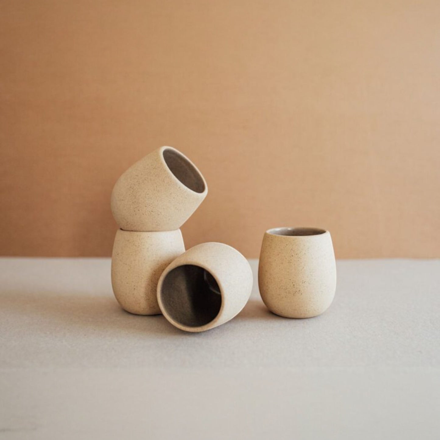 Several round stoneware cups in sand colors arranged in a row showing their sculptural shape.