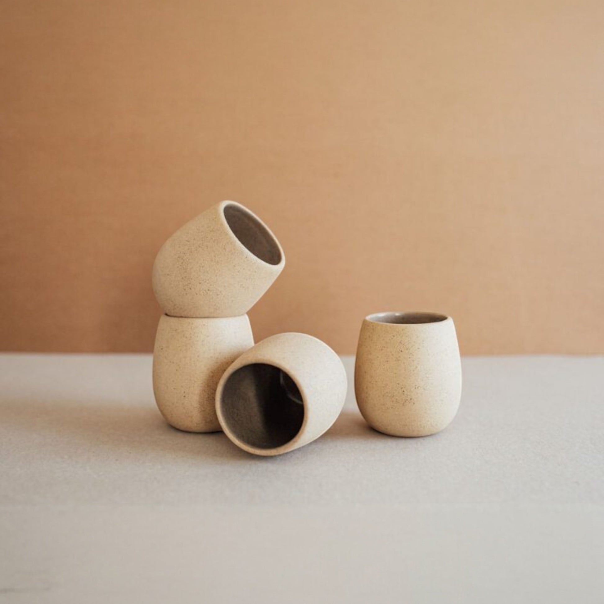 Several round stoneware cups in sand colors arranged in a row showing their sculptural shape.