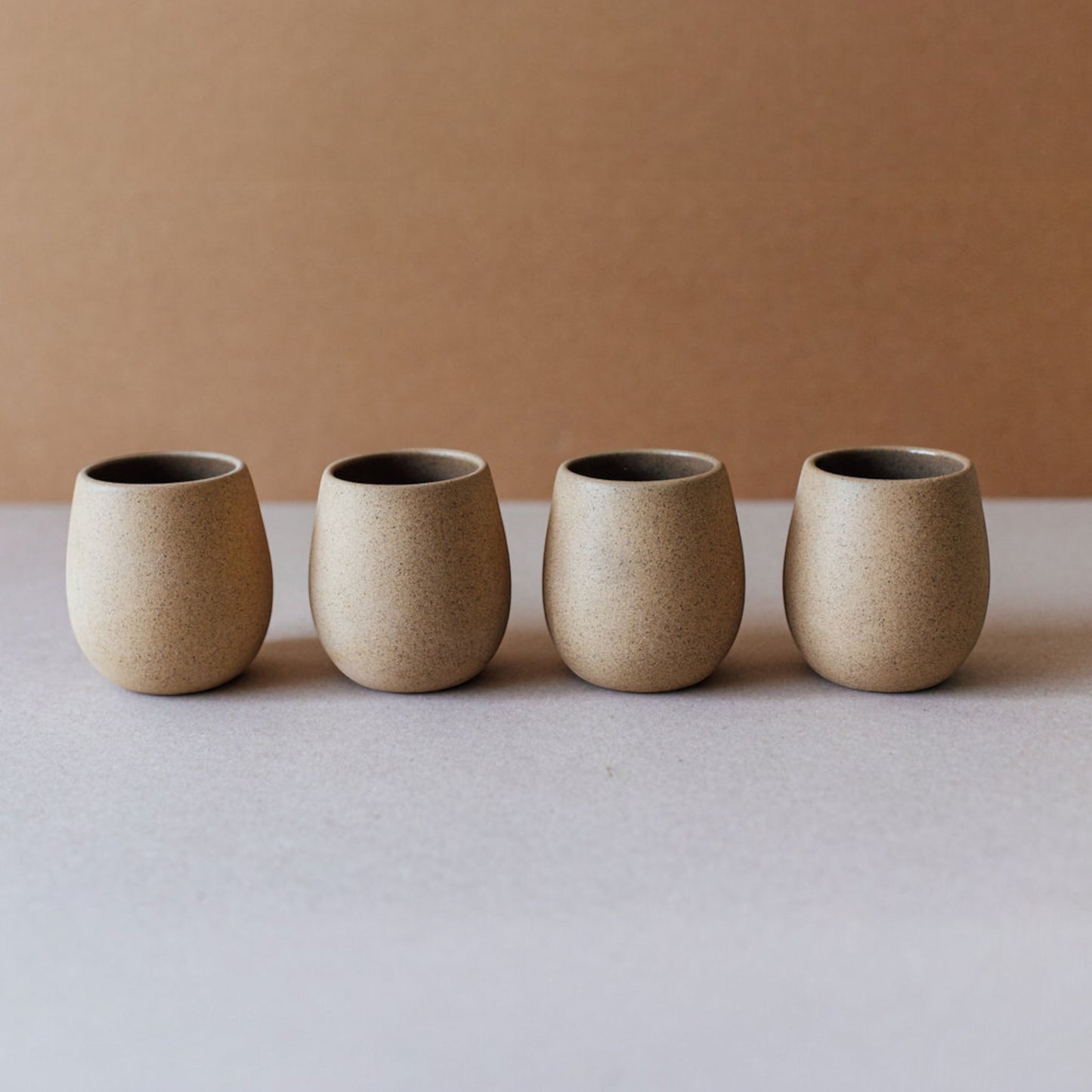 Round stoneware cup with a smooth matte exterior in a warm sand tone, sitting on a neutral backdrop