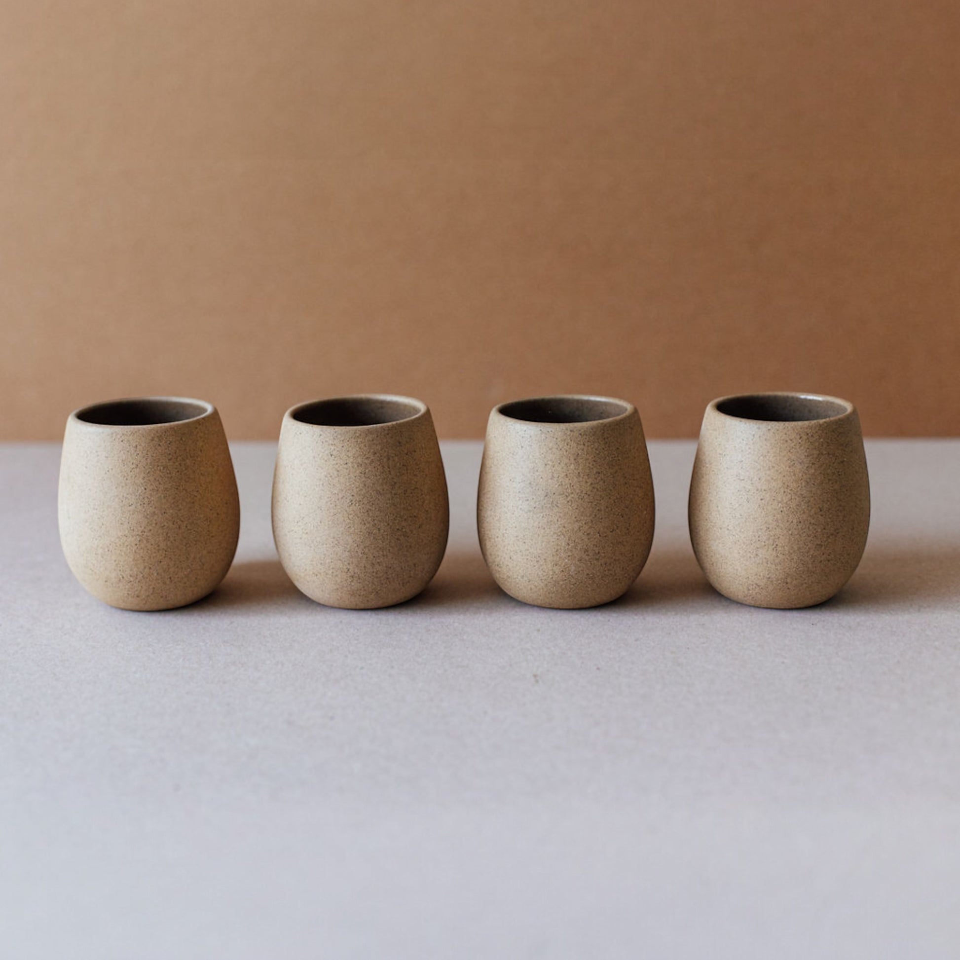 Round stoneware cup with a smooth matte exterior in a warm sand tone, sitting on a neutral backdrop