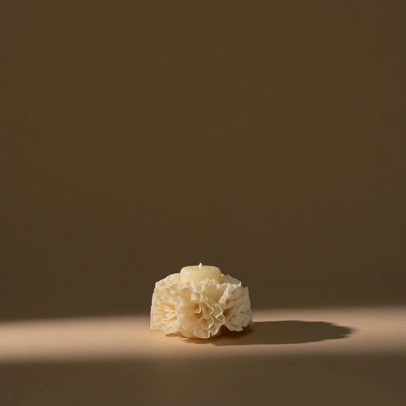 Ivory carved beeswax floral candle styled on dark neutral background with soft shadow