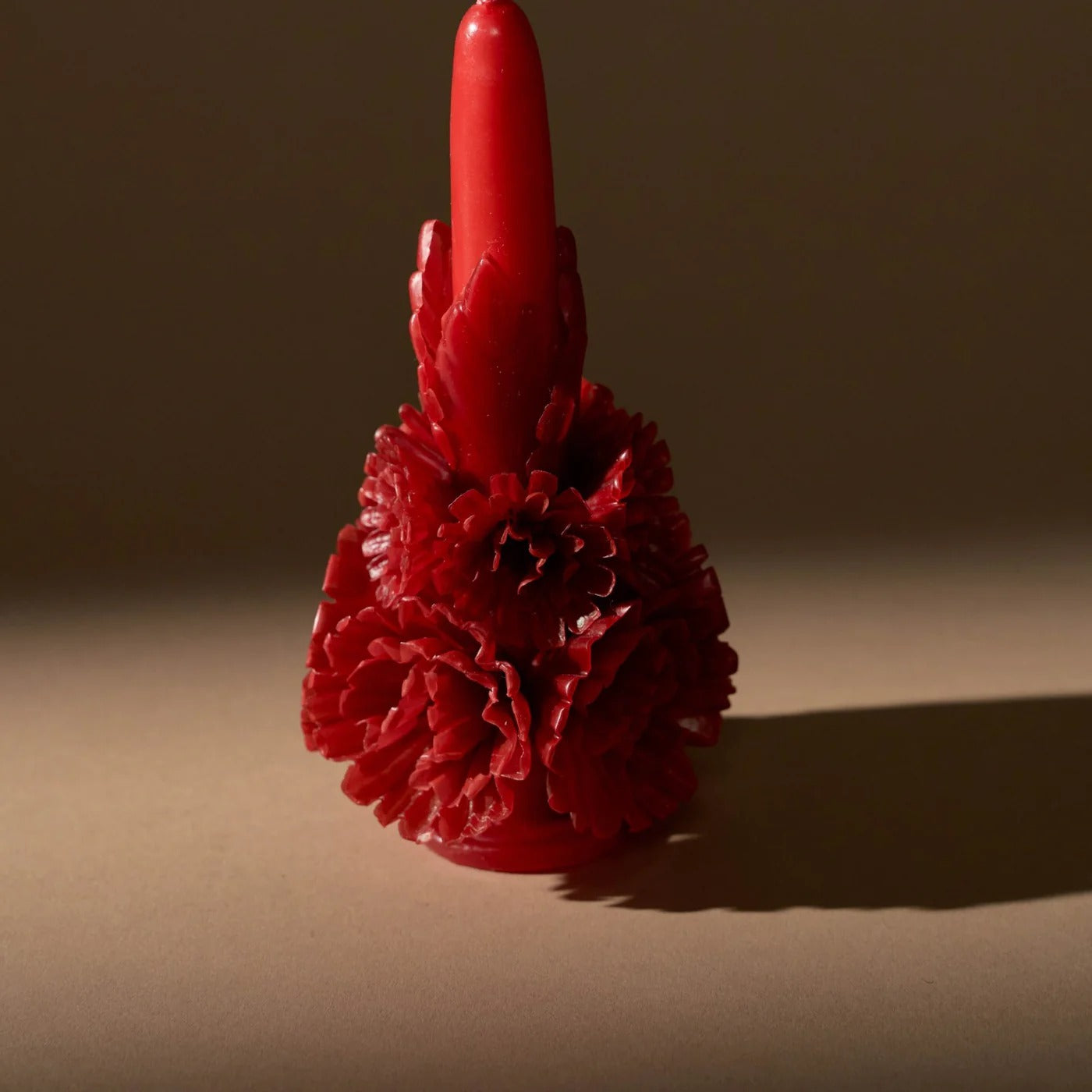 Red carved beeswax floral candle with dramatic lighting on neutral background