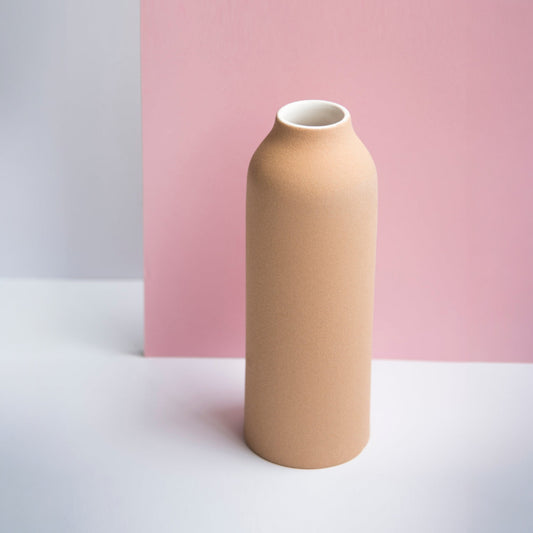 Tall terracotta urn vase with white glaze on a neutral pink background.