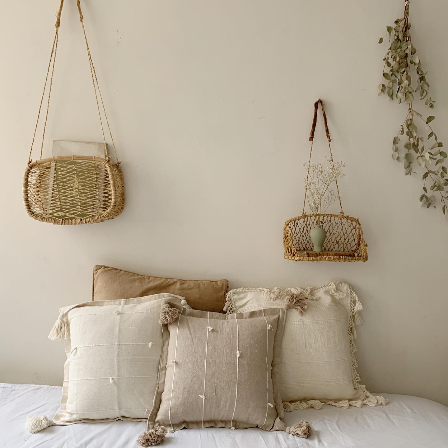 Decorative pillows on a bed with two jonote hanging baskets displayed on the wall with dried plants.