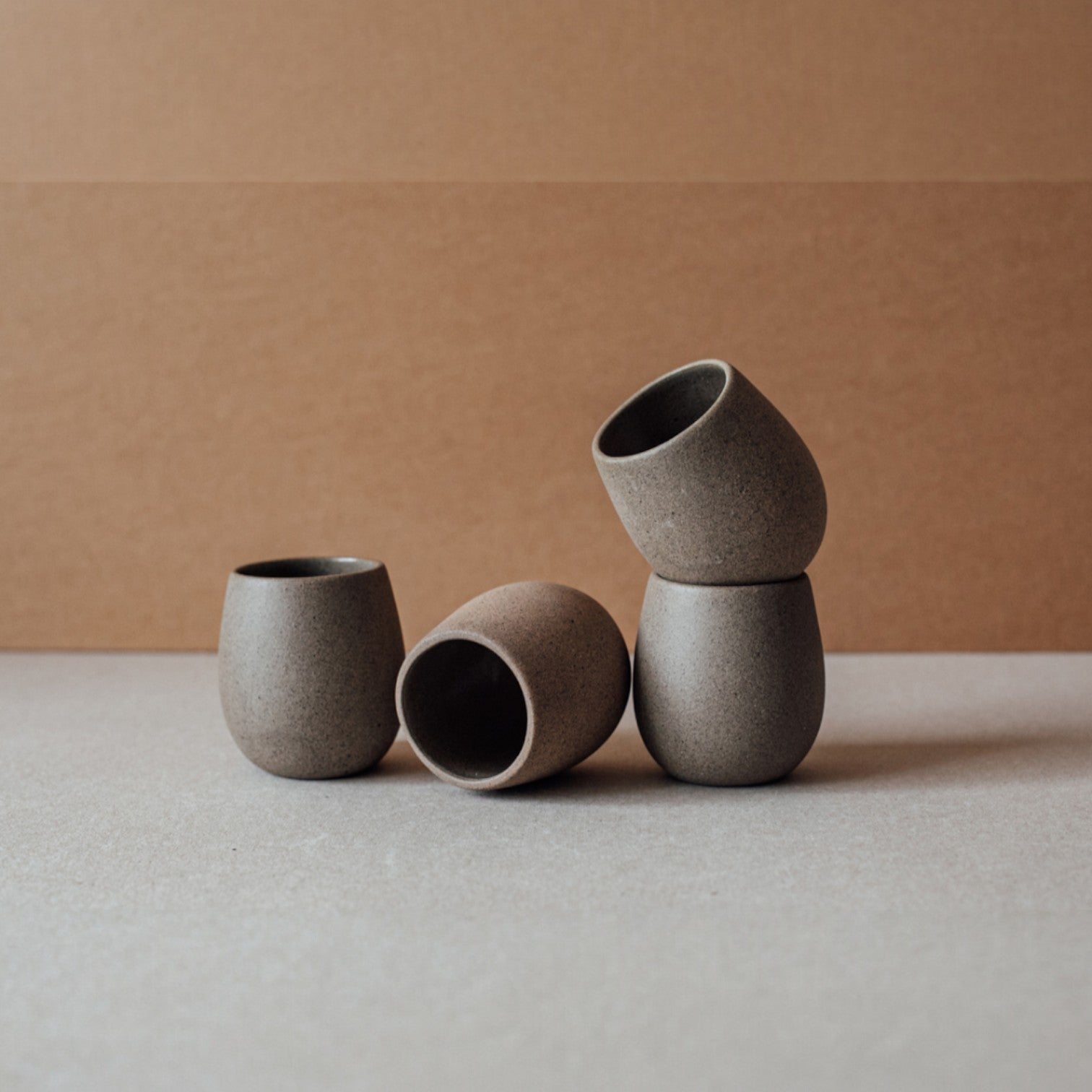 Round stoneware cup with a smooth matte exterior in chocolate tone, sitting on a neutral backdrop