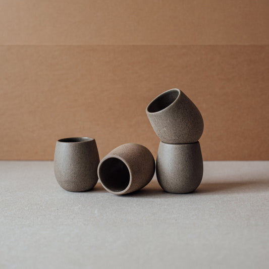 Round stoneware cup with a smooth matte exterior in chocolate tone, sitting on a neutral backdrop