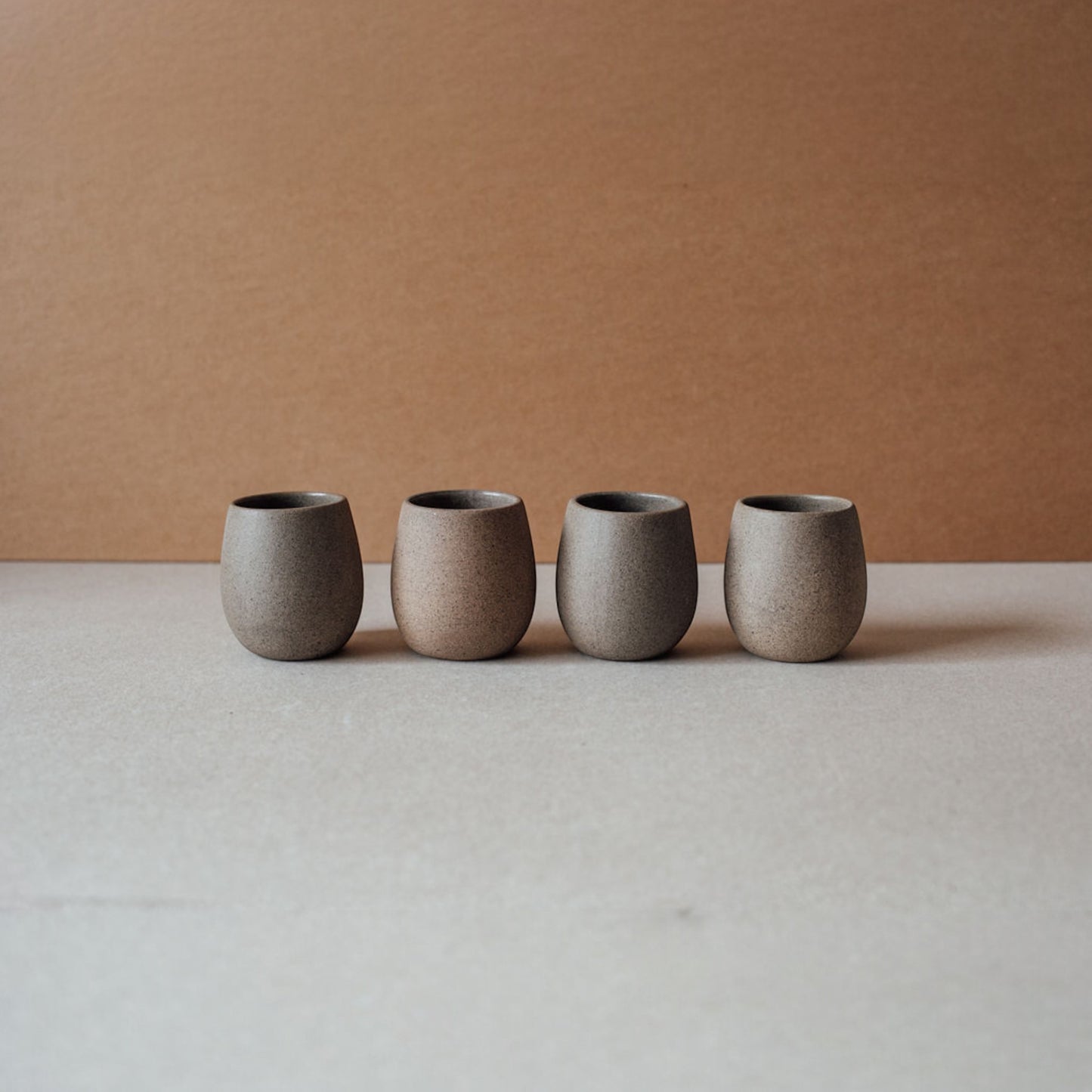 Several round stoneware cups in chocolate colors arranged in a row showing their sculptural shape.