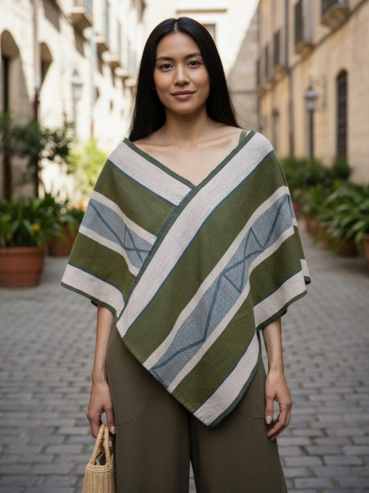 Model wearing a handwoven Mexican Quexquémetl poncho in olive and sand stripes, crafted in Cuetzalan, Puebla.