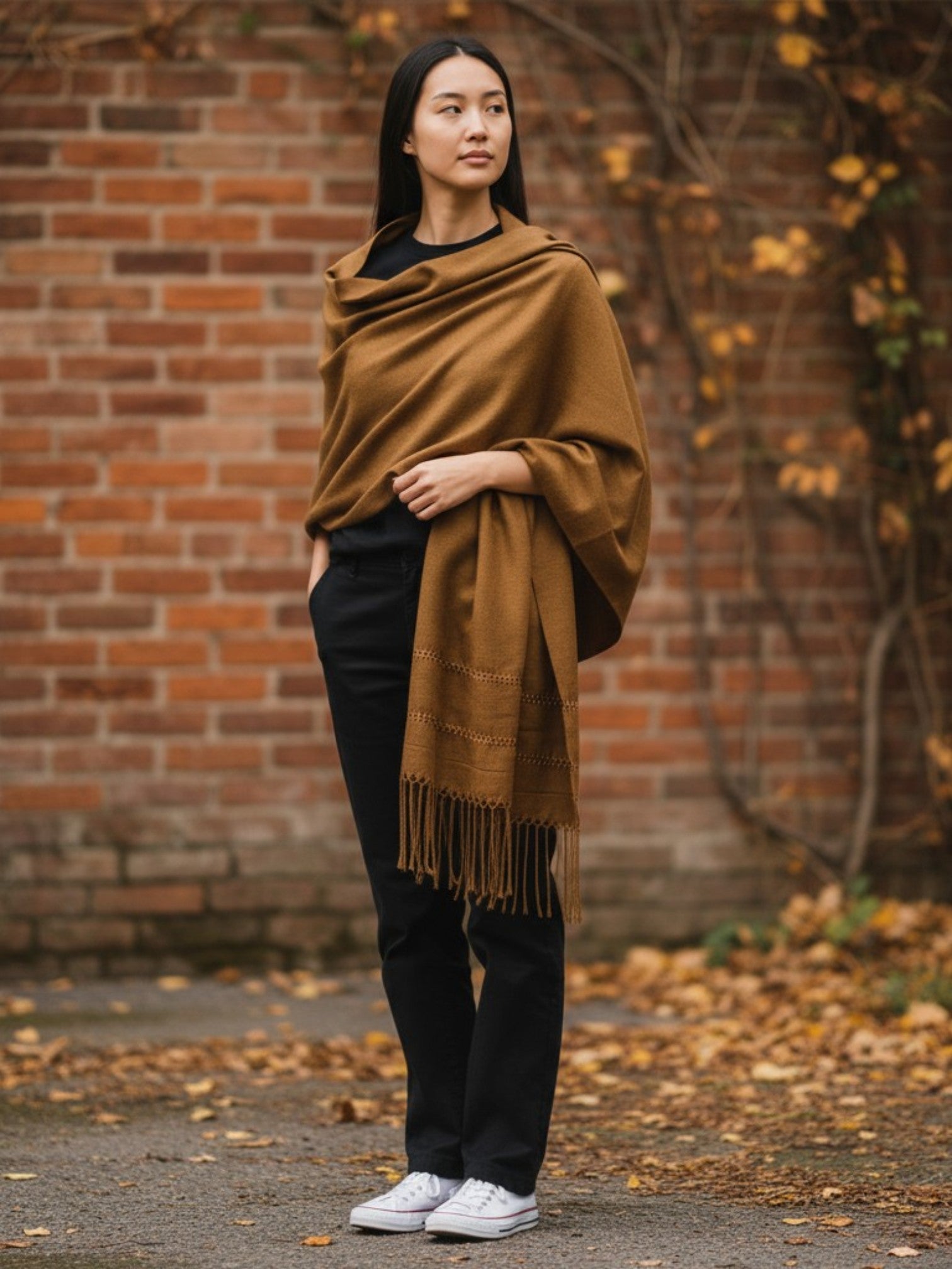Woman wearing a handwoven silk-blend rebozo shawl in golden, standing against a brick wall