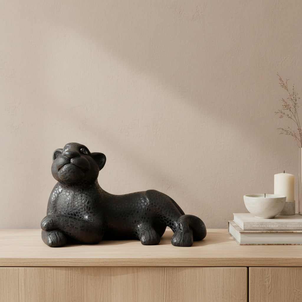 Black clay jaguar sculpture resting on a wooden cabinet with books and minimalist décor against a neutral wall