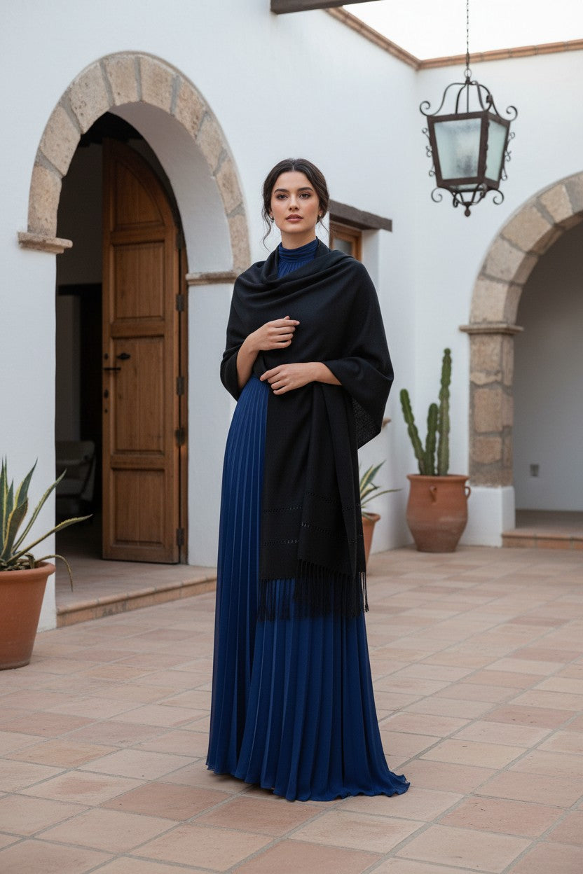 oman wearing a black handwoven shawl over a royal blue evening gown, standing in a Spanish-style courtyard with arches and terracotta pots