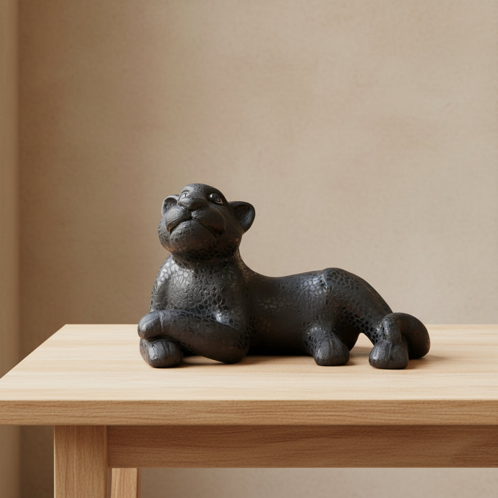 Black clay jaguar sculpture resting on a wooden table against a beige wall