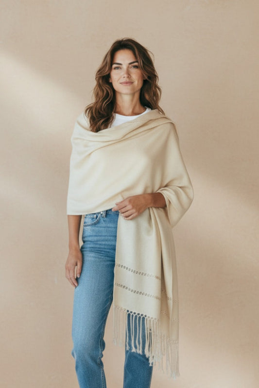 Model wearing an ivory handwoven Mexican shawl with delicate woven detailing and fringe, styled in a minimalist neutral setting