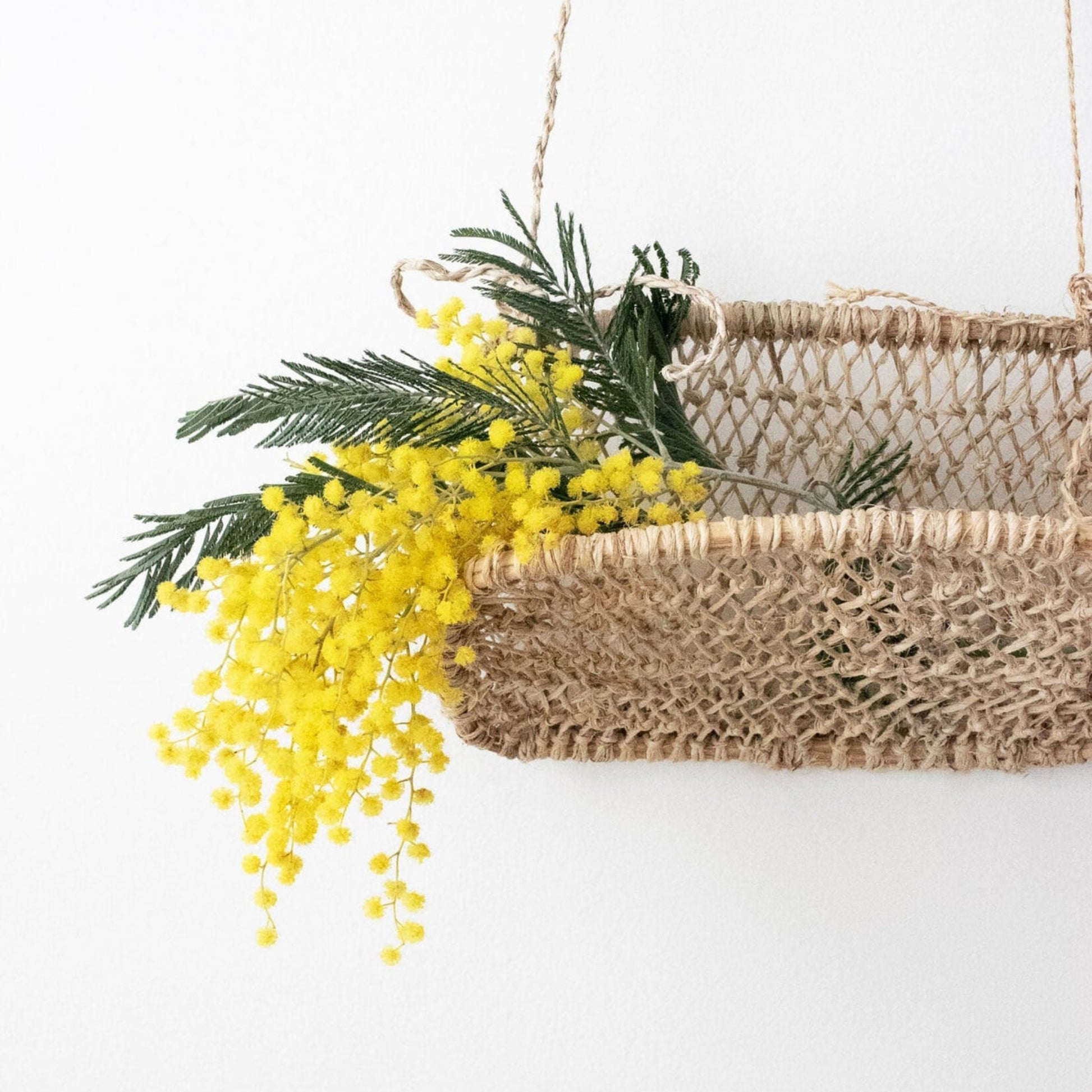 Close-up of a handwoven jonote hanging basket decorated with yellow flowers and green foliage.